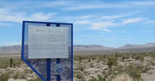 Sign marking the Nevada Test Site, with desert landscape and mountains in the background.