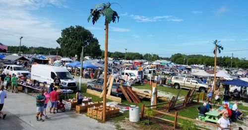 A bustling outdoor market with vendors, tents, and palm trees, filled with people shopping and socializing.