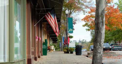 A quaint street lined with shops, featuring an American flag, colorful banners, and autumn foliage.