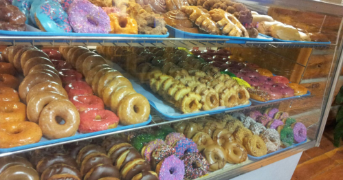 A display case filled with a variety of colorful donuts, including glazed, frosted, and sprinkled options.