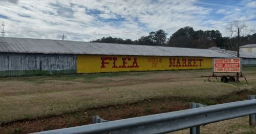 A colorful sign for "Mountain Top Flea Market" on a building, with grassy area and cloudy sky in the background.