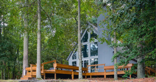 A modern cabin with large windows, surrounded by trees and featuring a wooden deck.