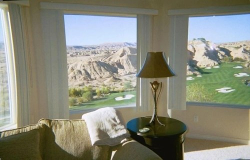 Cozy interior with a lamp and a table, featuring large windows showcasing a scenic golf course and rocky landscape outside.