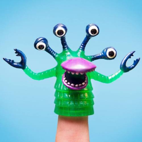 A colorful, multi-eyed monster toy with claws, perched on a finger against a blue background.