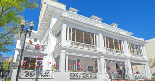 A white, historic building with large windows and decorative balconies, set against a clear blue sky.