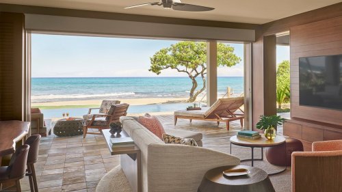 A modern living room with ocean views, featuring comfortable seating and a patio leading to the beach.
