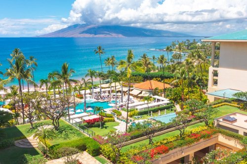 A vibrant tropical resort with pools, palm trees, and ocean views, set against a backdrop of mountains and blue skies.