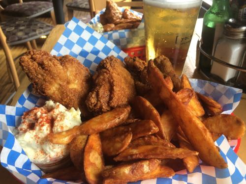 A basket of crispy fried chicken wings with seasoned potato wedges and a side of creamy dip, accompanied by a beer.