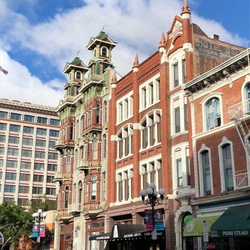 Historic buildings with ornate architecture under a blue sky, showcasing a mix of styles and vibrant storefronts.