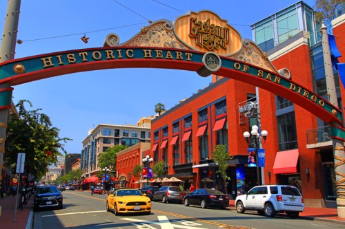 Colorful archway reading "Historic Heart of San Diego" over a bustling street with shops and cars.