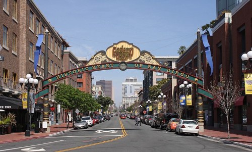Colorful archway reading "Historic Heart of San Diego" over a street lined with buildings and parked cars.