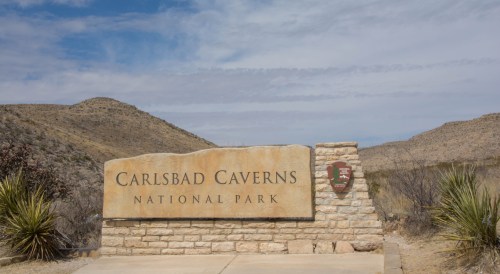 Sign for Carlsbad Caverns National Park with desert landscape and blue sky in the background.