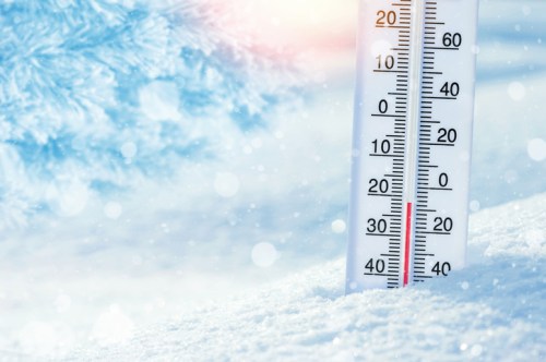 A close-up of a thermometer in snow, showing a temperature below freezing, with a soft, snowy background.