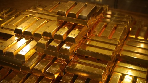 Stacks of shiny gold bars arranged closely together, reflecting light in a warm, golden hue.