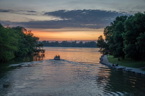 A serene sunset over a lake, with a boat gliding through the water and trees lining the shore.