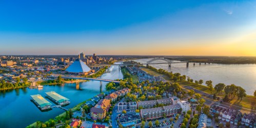 Aerial view of a city skyline at sunset, featuring a river, bridges, and a pyramid-shaped building.