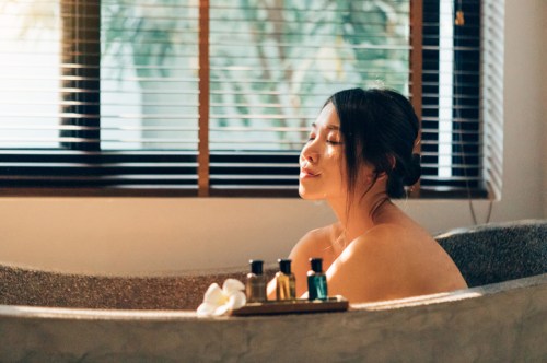 A woman relaxes in a bathtub, enjoying a serene moment with sunlight streaming through the window.
