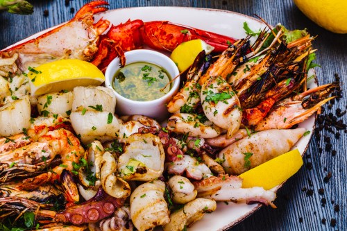 A vibrant seafood platter featuring shrimp, scallops, crab, and lemon wedges, served with a dipping sauce.