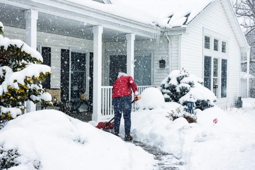 A person shoveling snow from a walkway in front of a house during a heavy snowfall.
