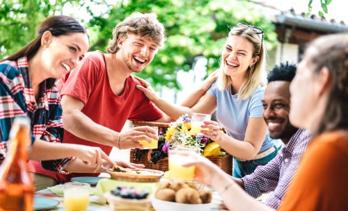 A group of friends enjoying a cheerful outdoor meal, laughing and toasting with drinks at a festive table.