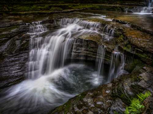 A serene waterfall cascades over rocky cliffs into a tranquil pool, surrounded by lush greenery.