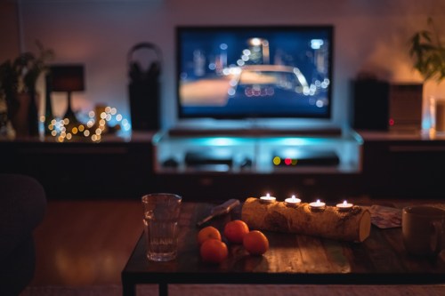 A cozy living room with a TV displaying a city scene, candles on a log, and fruit on a coffee table.