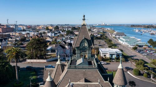 Aerial view of a coastal town featuring a historic building, palm trees, and a marina in the background.