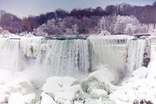 A snowy landscape featuring a frozen waterfall surrounded by trees, creating a serene winter scene.