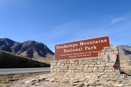 Sign for Guadalupe Mountains National Park, with mountains and clear blue sky in the background.