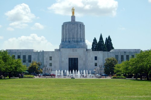 Oregon State Capitol building with a golden statue on top, surrounded by green lawns and a fountain in the foreground.