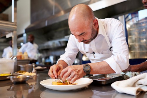 A chef carefully plating a dish in a professional kitchen, focused on presentation.