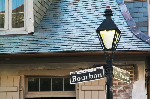 Street signs for Rue Bourbon and St. Philip with a vintage lamp post in front of a building with a slate roof.