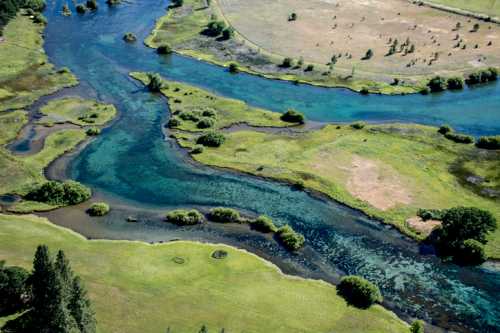 Aerial view of a winding river surrounded by lush greenery and open fields, showcasing vibrant blue and green waters.