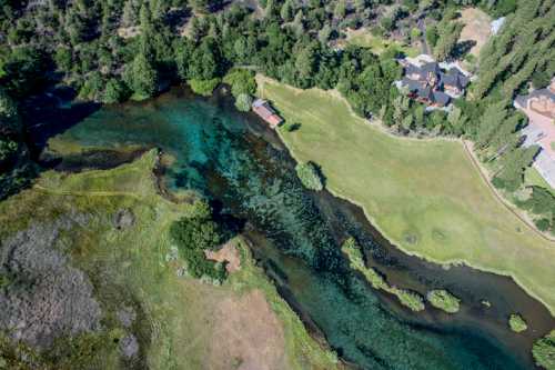 Aerial view of a lush green landscape with a winding river, surrounded by trees and a few houses nearby.