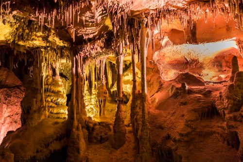 A colorful cave interior with stalactites and stalagmites illuminated by warm lighting.