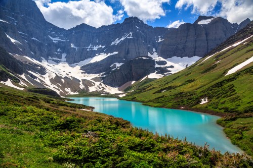 A serene mountain landscape featuring a turquoise lake surrounded by lush greenery and snow-capped peaks under a blue sky.