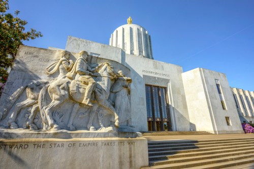 Exterior view of a grand building with a dome, featuring a sculptural relief of horsemen at the entrance.