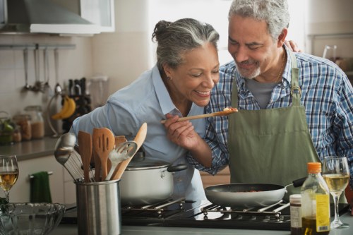 A happy older couple cooking together in a kitchen, sharing a playful moment with a spoon.