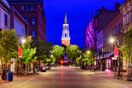 A quiet street at dusk, lined with trees and buildings, featuring a clock tower in the background.