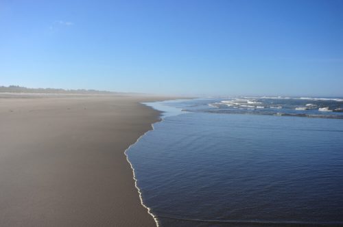 A serene beach scene with gentle waves lapping at the shore under a clear blue sky.
