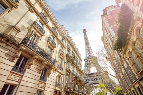 View of the Eiffel Tower framed by historic Parisian buildings under a bright sky.