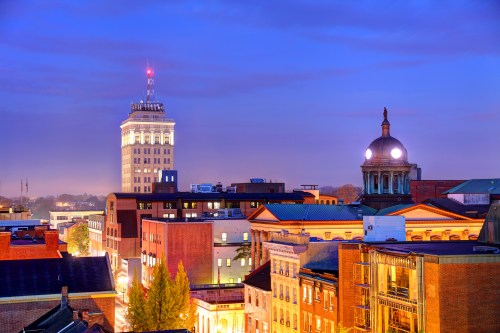 A city skyline at dusk featuring historic buildings and a tall tower illuminated against a twilight sky.