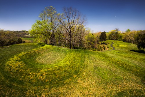 A scenic view of rolling green hills with trees under a clear blue sky, showcasing winding paths through the landscape.