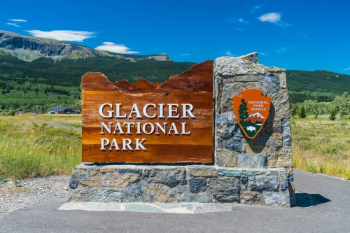Sign for Glacier National Park, featuring a wooden plaque and the National Park Service emblem against a scenic backdrop.