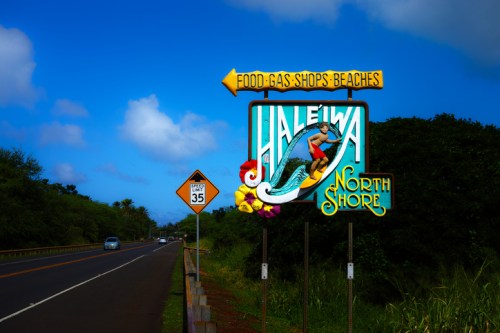 Colorful sign for Haleiwa, North Shore, with directions to food, gas, shops, and beaches, set against a blue sky.
