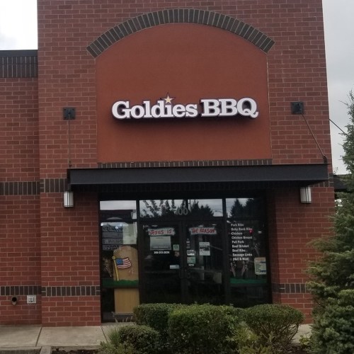 Sign for Goldie's BBQ on a brick building, featuring a large logo and a welcoming entrance.