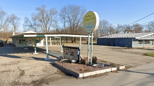 A small, vacant diner with a sign reading "New Era Canteen Café" and a cracked parking lot under a clear blue sky.