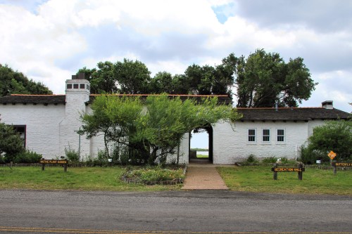 A white building with a garden, featuring signs for "Native Plant Garden" and "Recreation Hall," under a cloudy sky.
