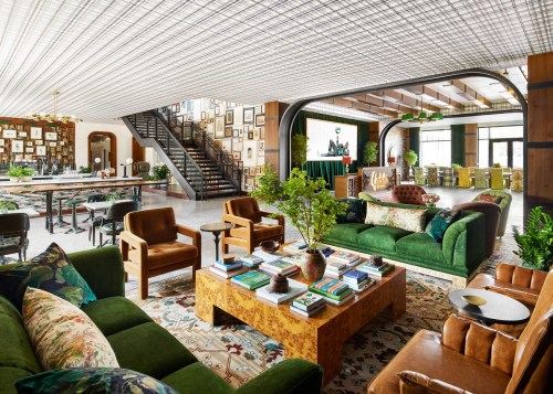 A stylish, modern lounge with green sofas, a wooden coffee table, and a gallery wall, featuring a staircase in the background.