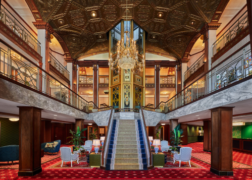 Elegant hotel lobby featuring a grand staircase, ornate ceiling, chandelier, and stylish seating areas.